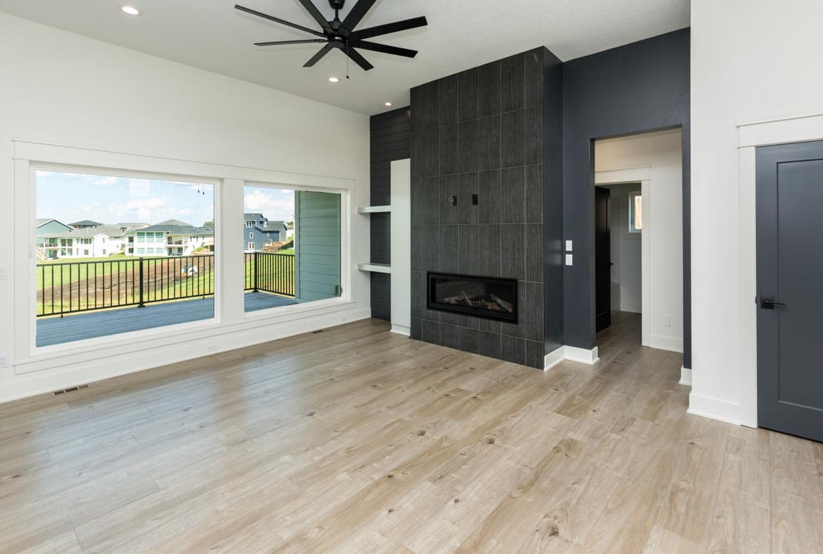 Interior view of a living room with large windows, a modern fireplace, and a black ceiling fan.