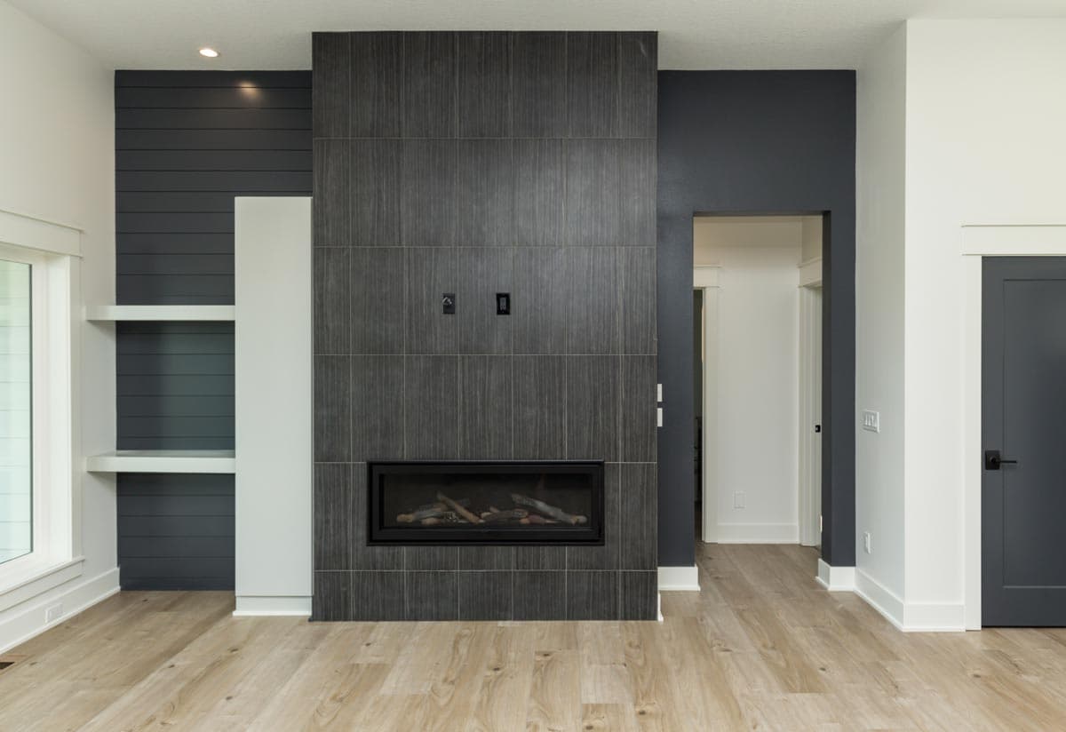 Contemporary living room with a floor-to-ceiling tiled fireplace surround, shiplap accent wall with shelves, and a dark gray door.