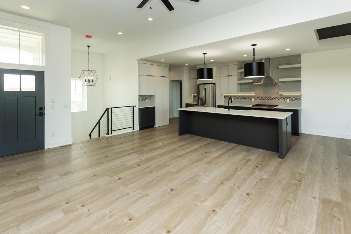 Open-concept living area with a modern kitchen featuring a large island, stainless steel appliances, and two pendant lights.