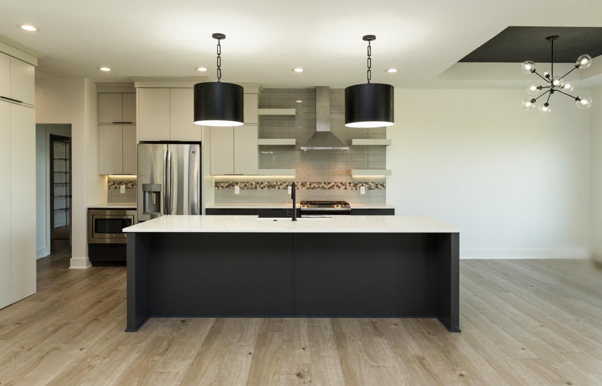 Modern kitchen with dark island, white countertops, stainless steel appliances, gas range, and pendant lighting.