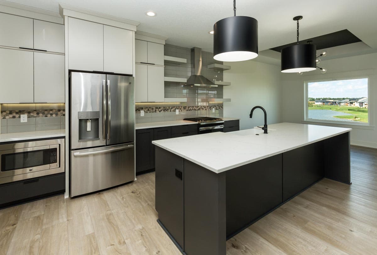 Modern kitchen with stainless steel appliances, large island, dark grey lower cabinets, and a tile backsplash.