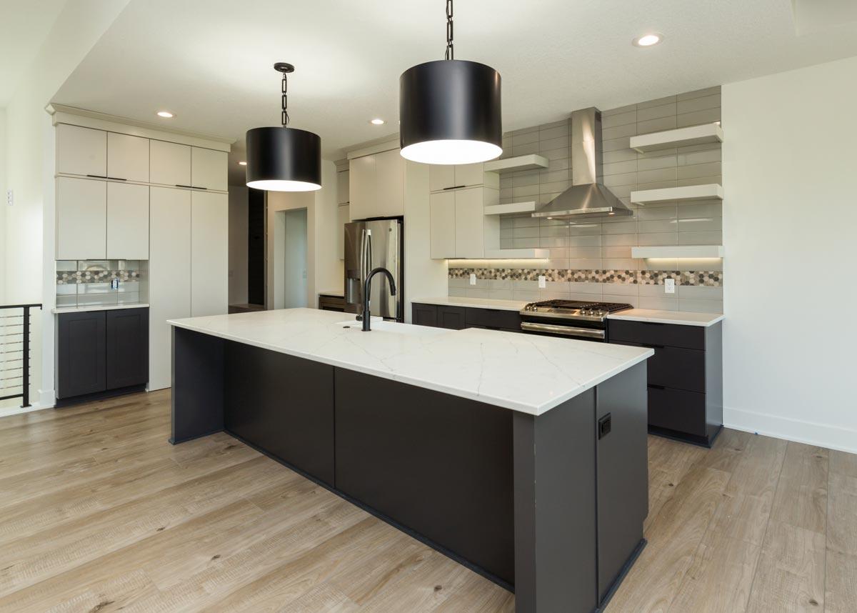 Modern kitchen with large island, stainless steel appliances, gas range, subway tile backsplash, and contemporary pendant lights.