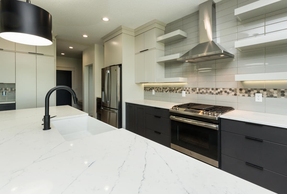 Modern kitchen featuring a large island with sink, stainless steel appliances, gas range, and minimalist cabinetry with integrated pulls.