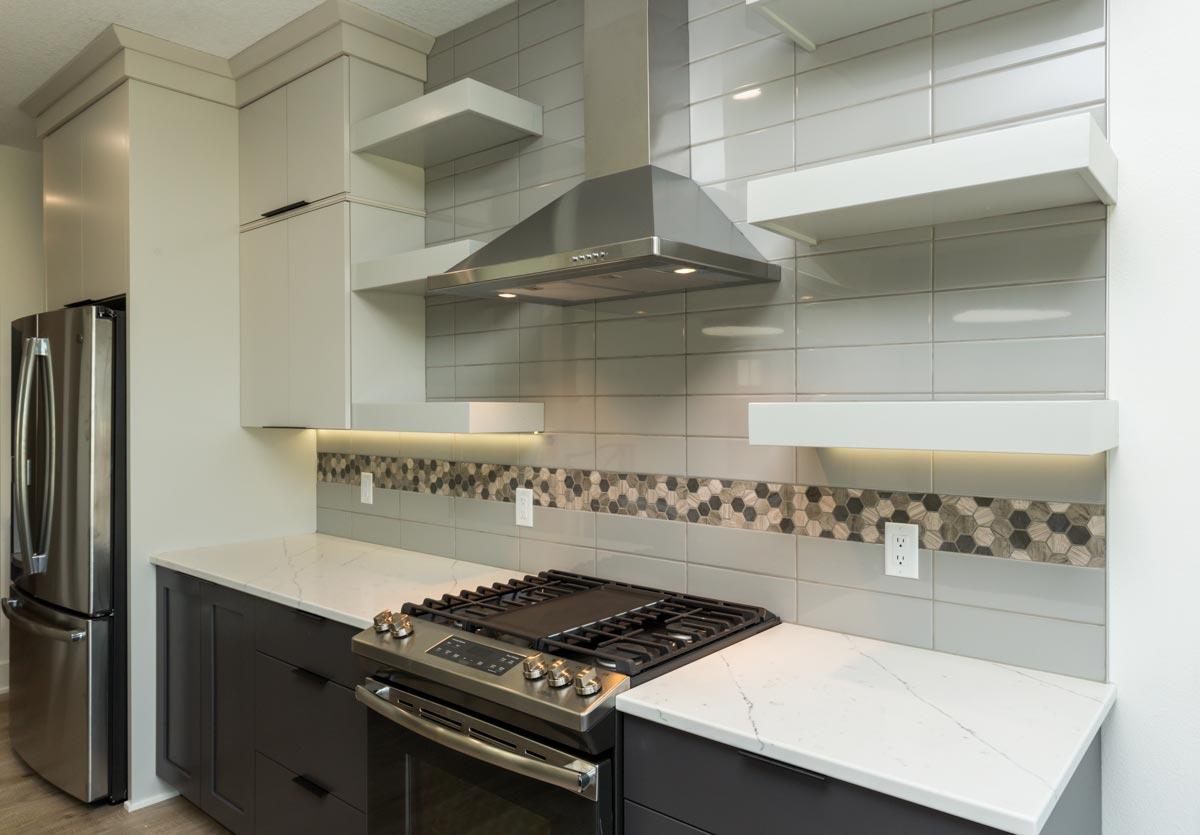 Kitchen interior with stainless steel gas range, contemporary cabinetry, and light gray subway tile backsplash with hexagonal mosaic accent.