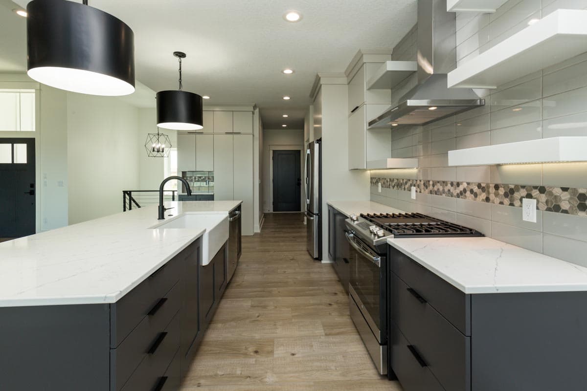 Modern kitchen with large island, farmhouse sink, stainless steel appliances, and contemporary pendant lights.