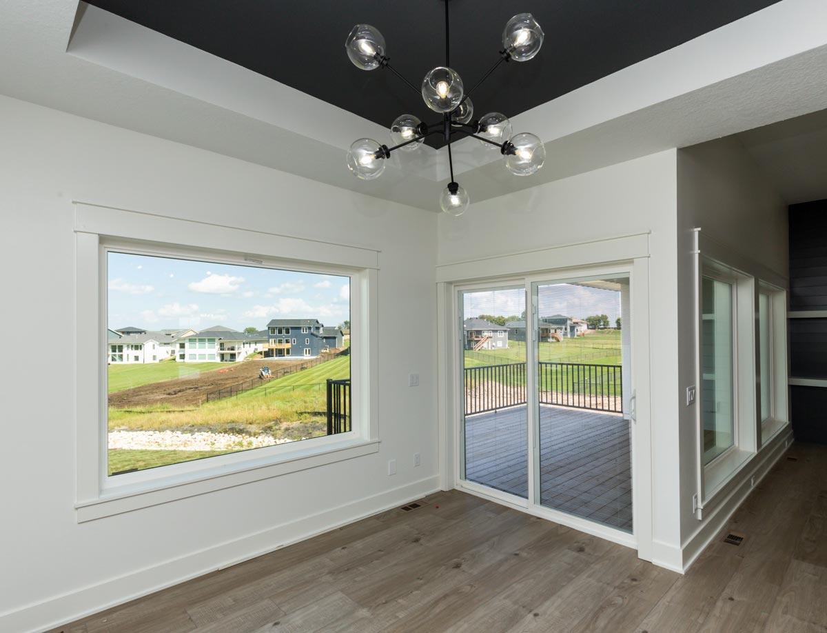 Interior view of a room with a black tray ceiling, large windows, sliding glass doors to a deck, and a modern chandelier.