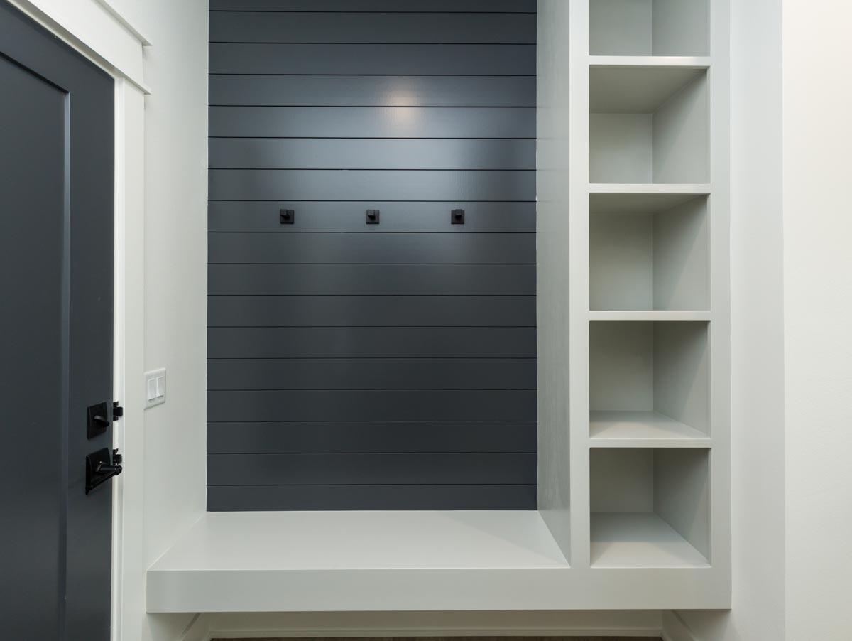 Mudroom with dark gray shiplap accent wall, built-in bench, and open shelving unit next to a dark gray door.