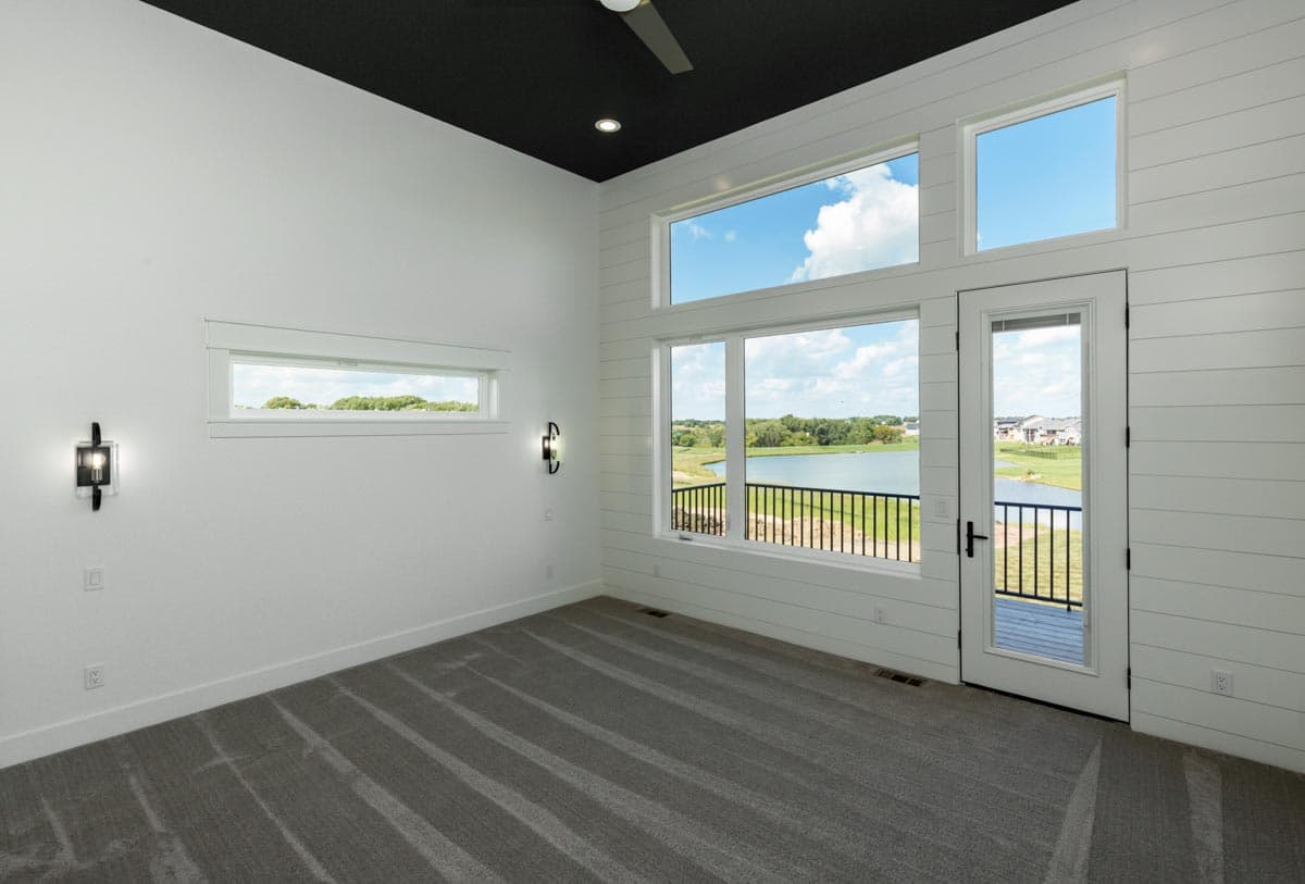 Interior view of room with horizontal shiplap accent wall, large windows, black ceiling, and balcony overlooking water.
