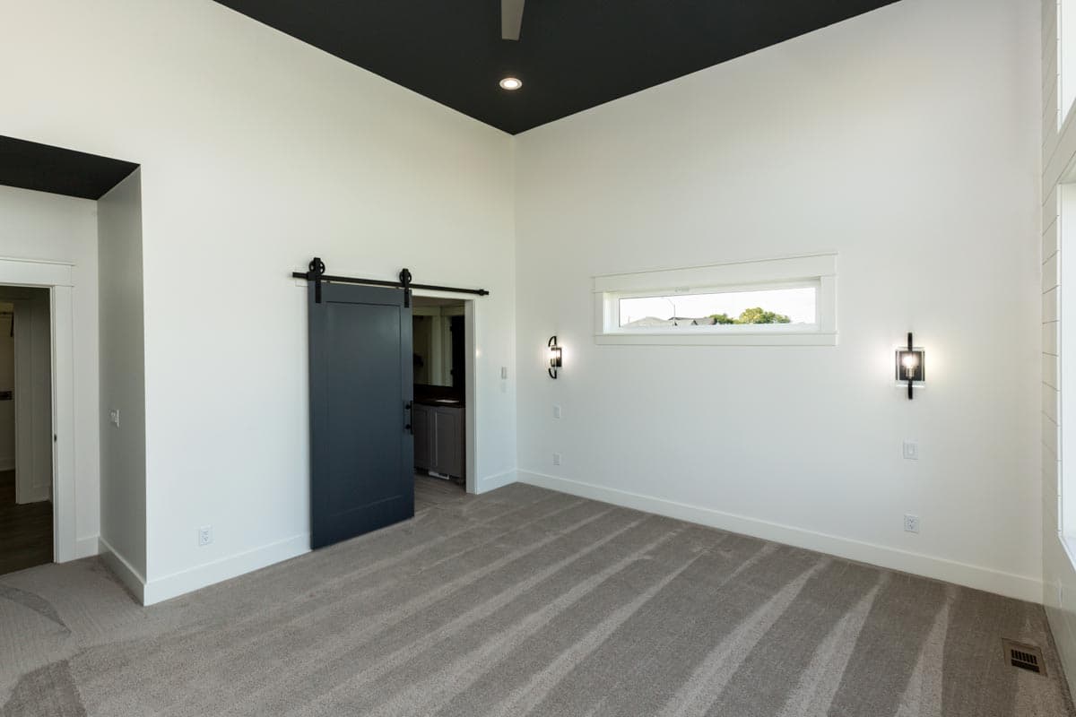 Interior view of a room with a dark grey barn door, a black ceiling, and a horizontal window with a black light fixture.