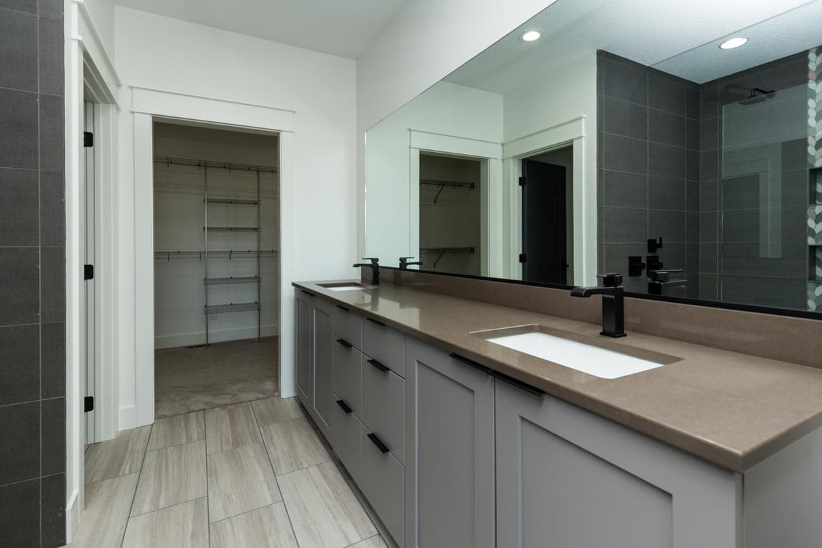 Bathroom with double vanity, walk-in closet, tiled shower, and wood-look tile flooring.