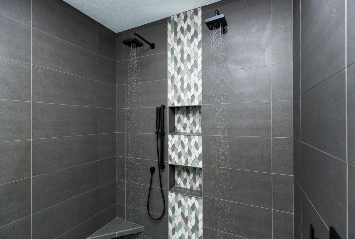 Modern bathroom with dual shower heads, built-in niches, and mosaic tile accent wall.