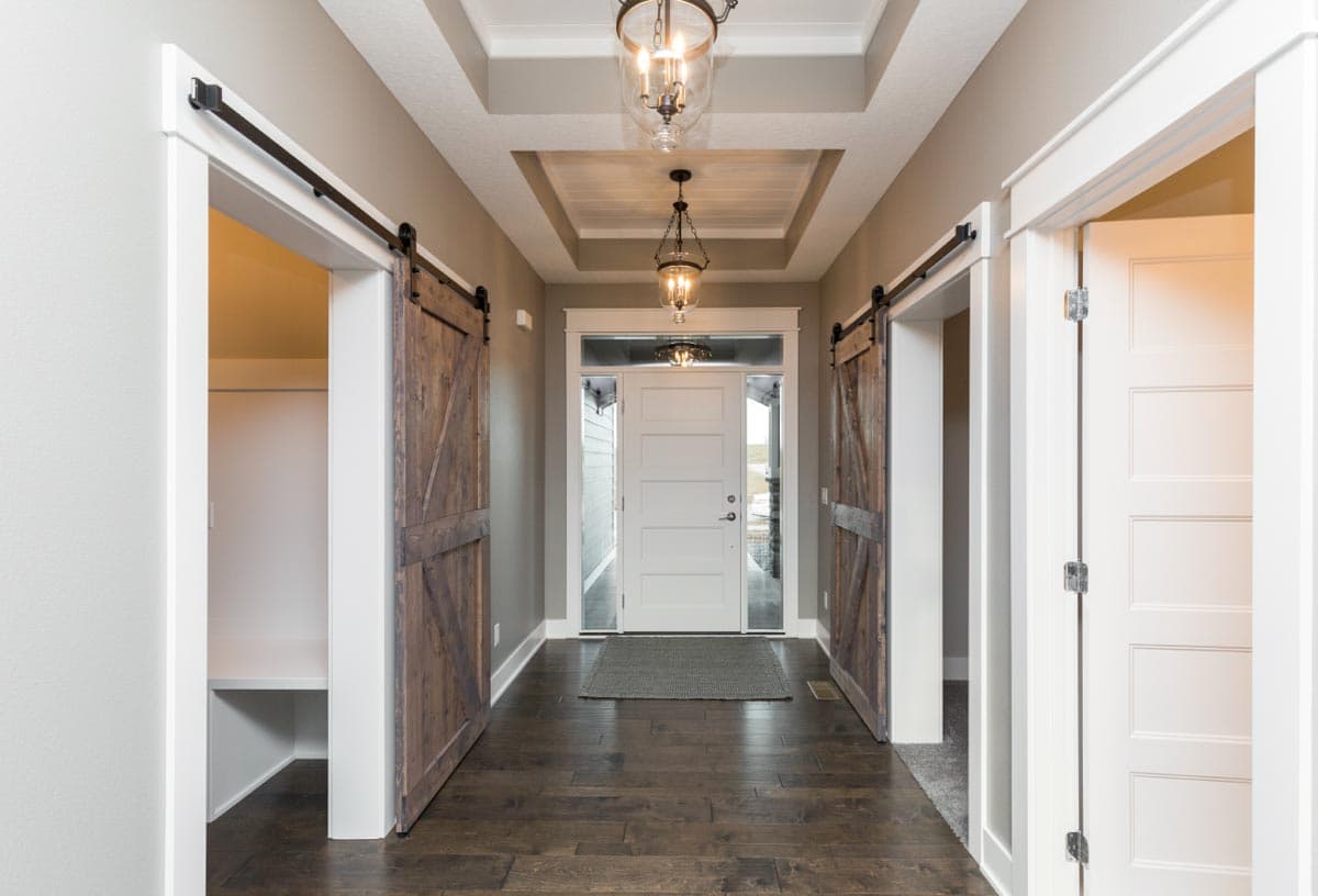 Interior view of entry with coffered ceiling, pendant lights, white front door, and two wooden barn doors.