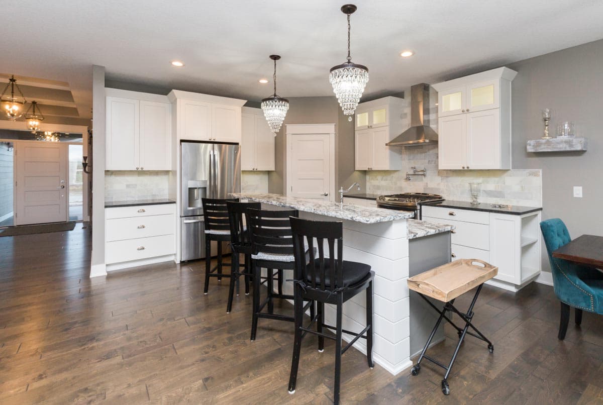 Kitchen with white cabinetry, granite island with seating, stainless steel appliances, and decorative pendant lights.