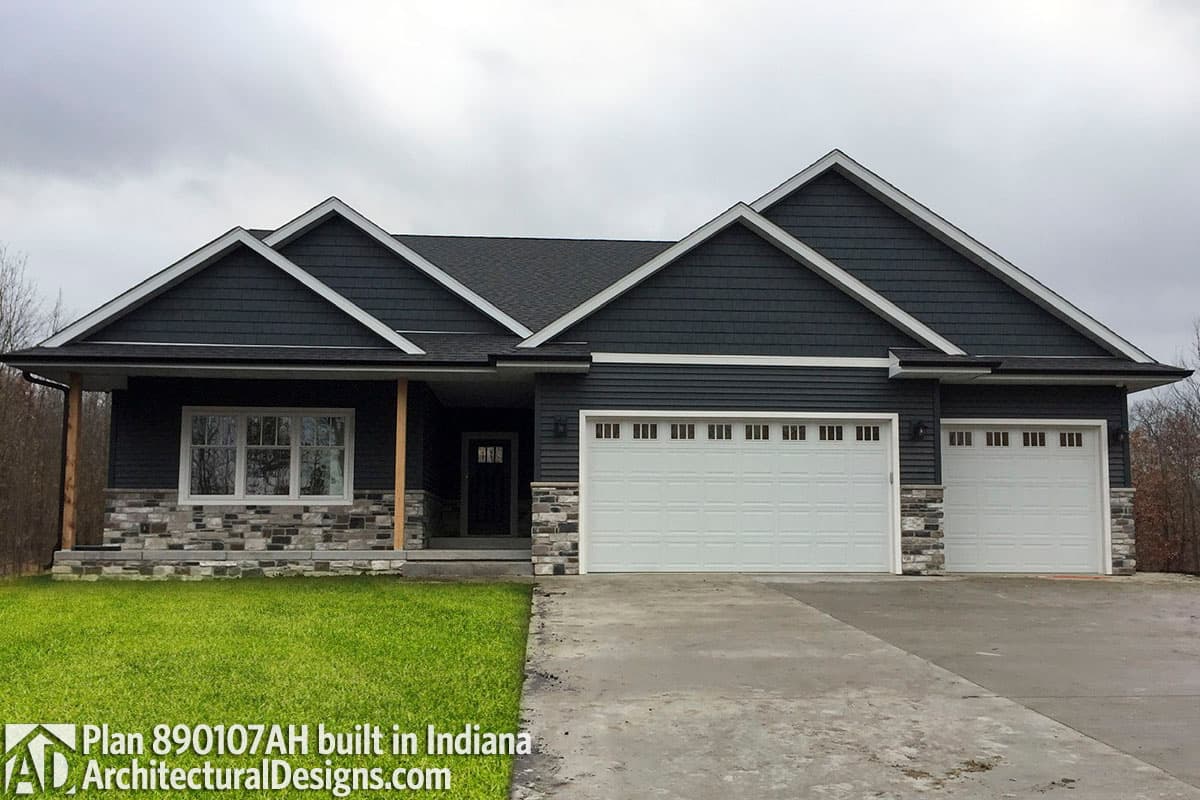 House plan exterior: Single-story modern home with a covered porch, stone base, dual gables, and a three-car garage.