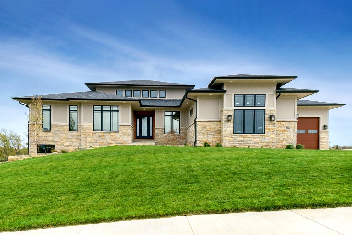 Modern house plan exterior with stone accents, multiple rooflines, large windows, and a wood garage door.