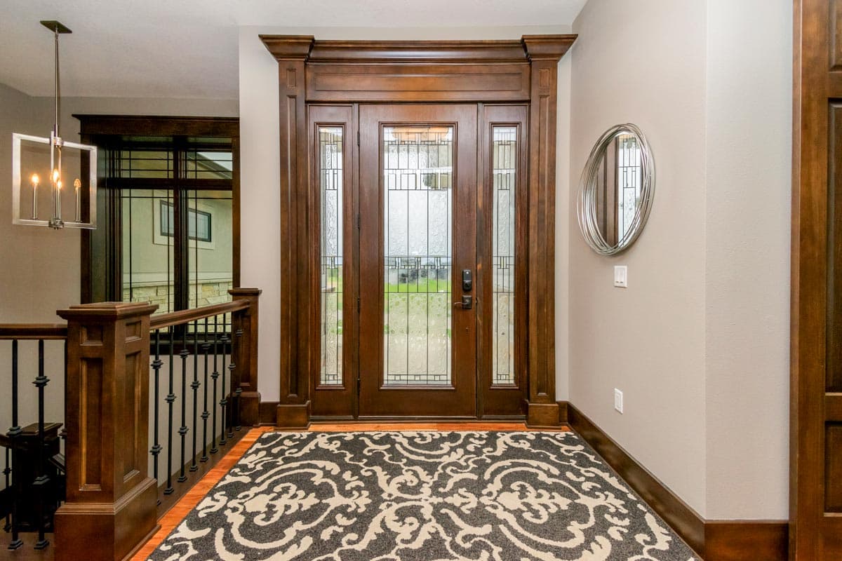 Interior entry foyer with double glass doors, stained wood trim, staircase railing, and modern chandelier.