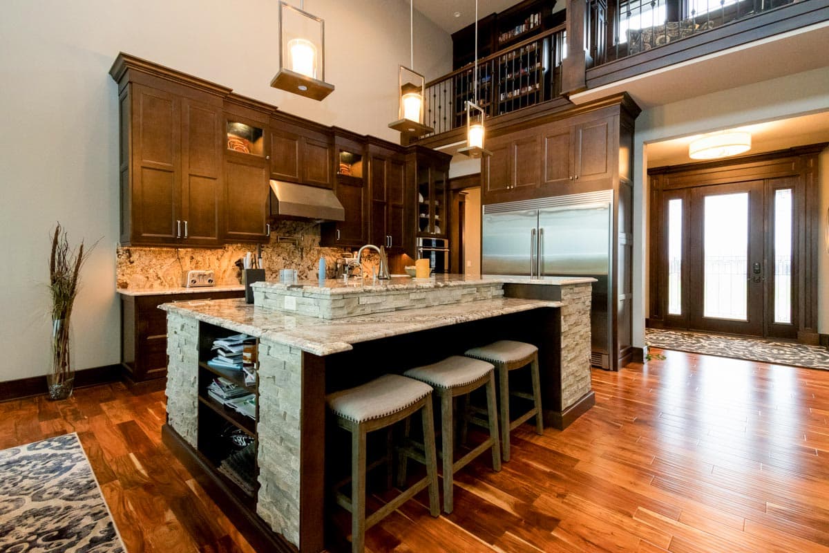 Kitchen with dark wood cabinetry, granite counters, stone-clad island with seating, and stainless steel refrigerator.