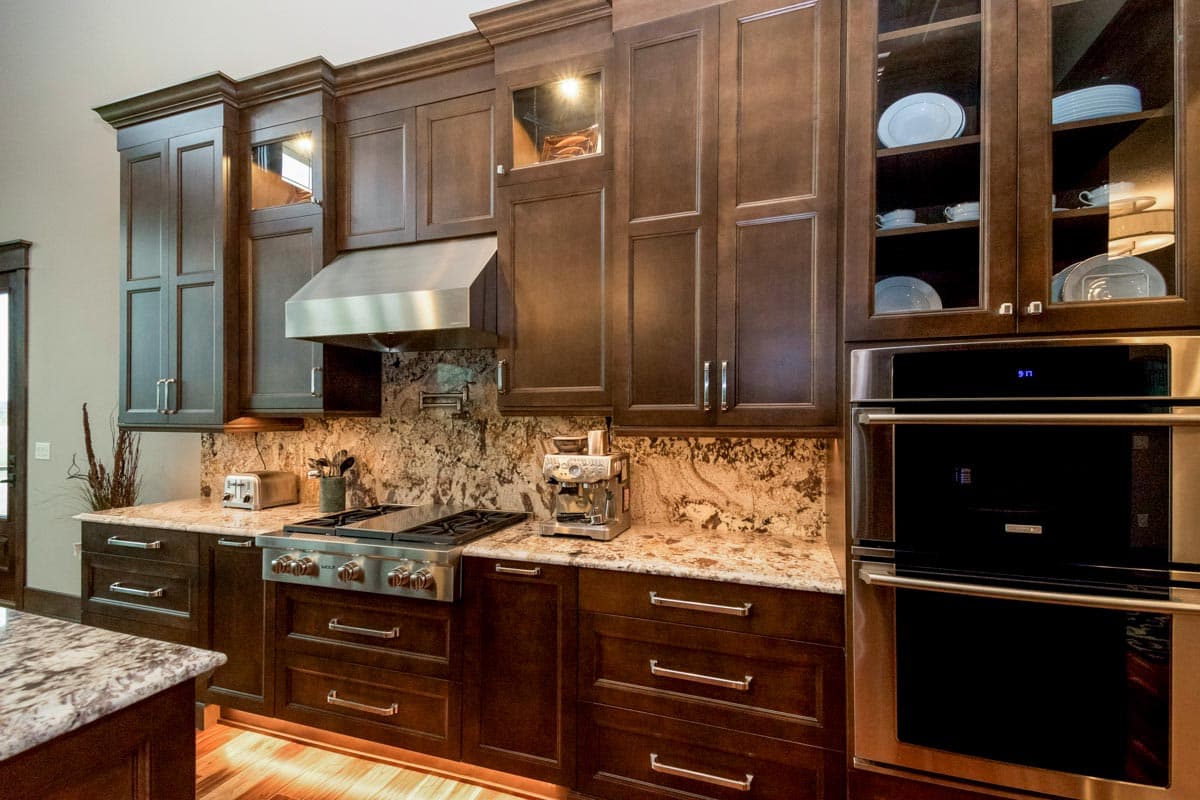 Kitchen with dark wood cabinets, stainless steel range hood, granite backsplash, and double wall ovens.