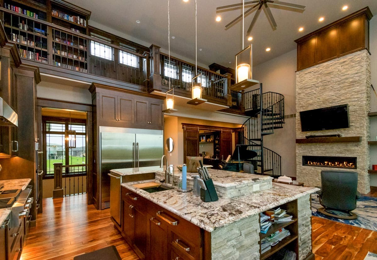 Open concept living space featuring a kitchen island, stone fireplace, spiral staircase, and extensive built-in shelving.