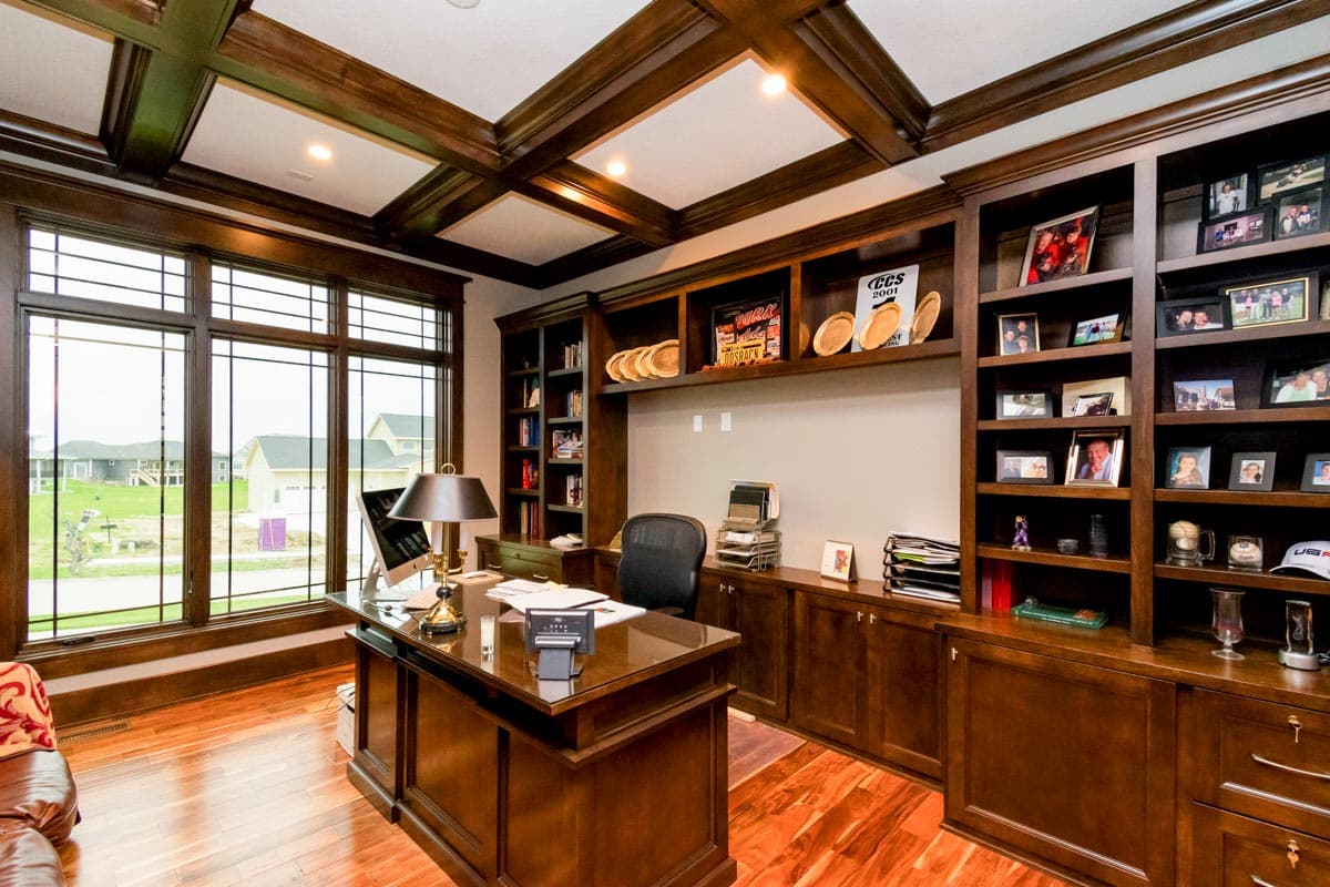 Office interior with coffered ceiling, built-in dark wood bookcases, and a large desk.