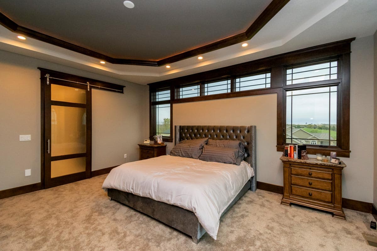 Primary bedroom with tufted headboard, decorative ceiling, and sliding glass door.