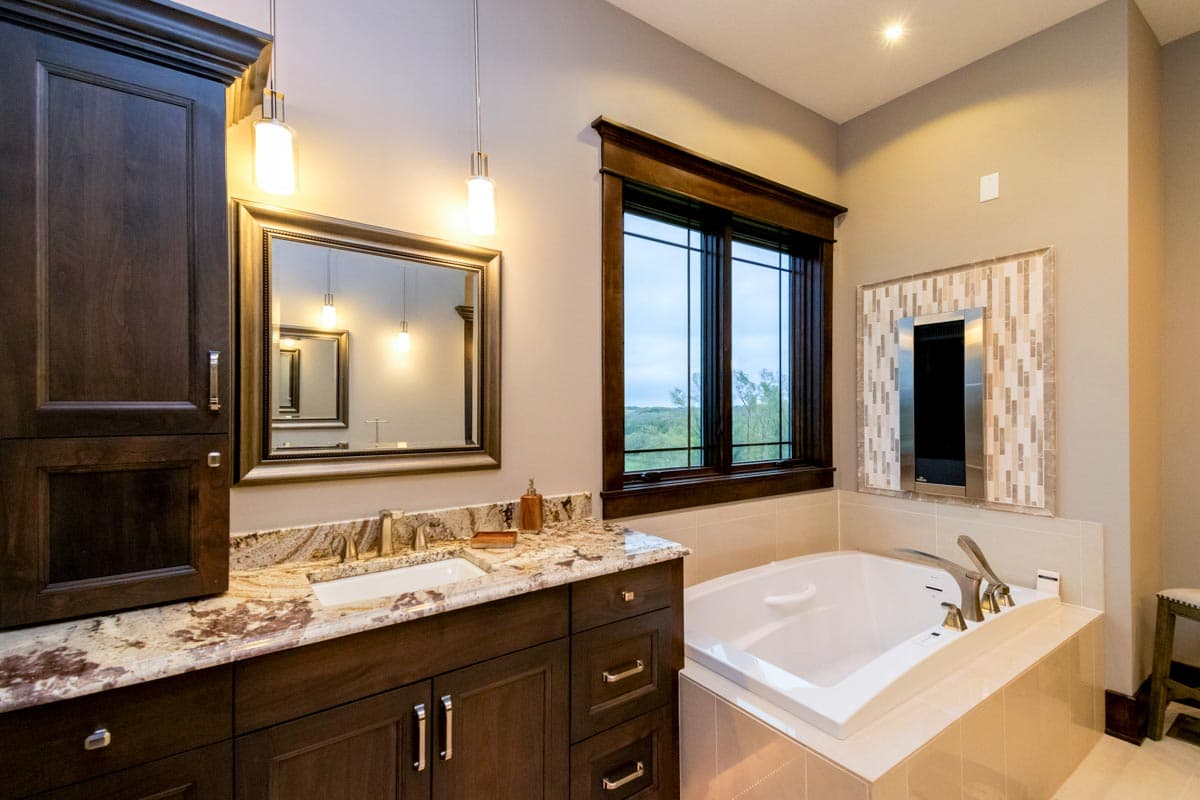 Bathroom with dark wood vanity, granite countertop, built-in tub, and decorative tile accent.