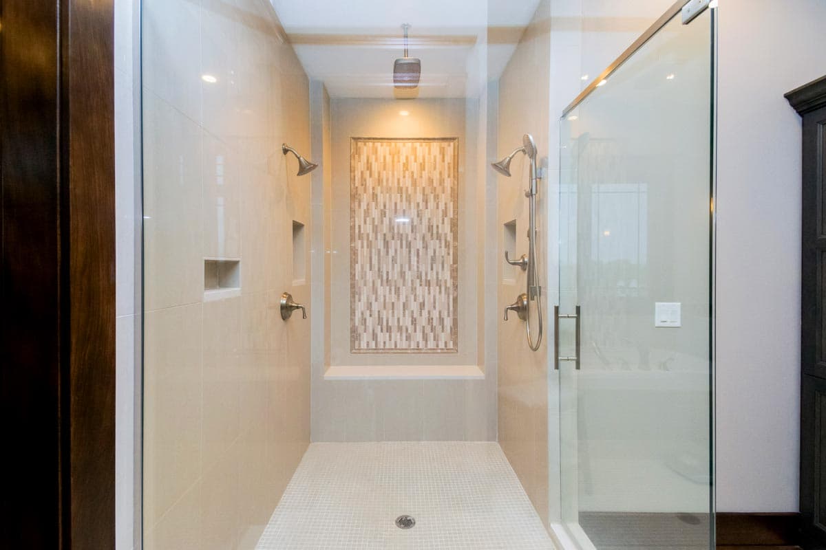 Master bathroom shower with dual shower heads, built-in niche, mosaic accent tile wall, and glass enclosure.