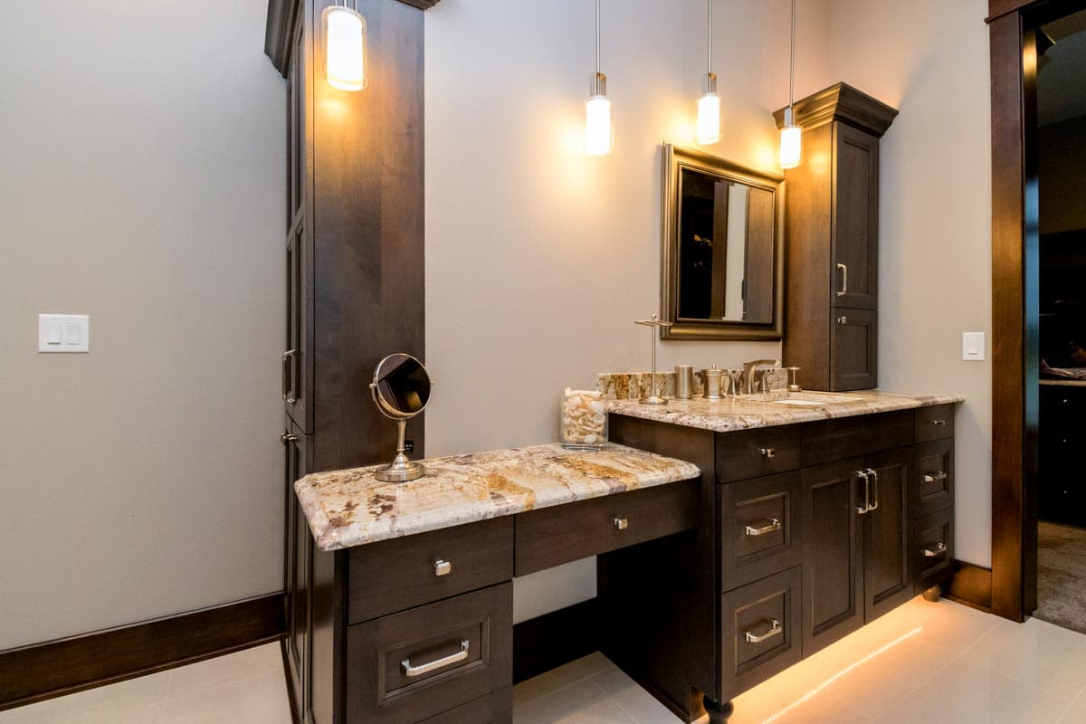 Dark wood vanity with granite countertop, double sinks, and integrated makeup area with mirror.