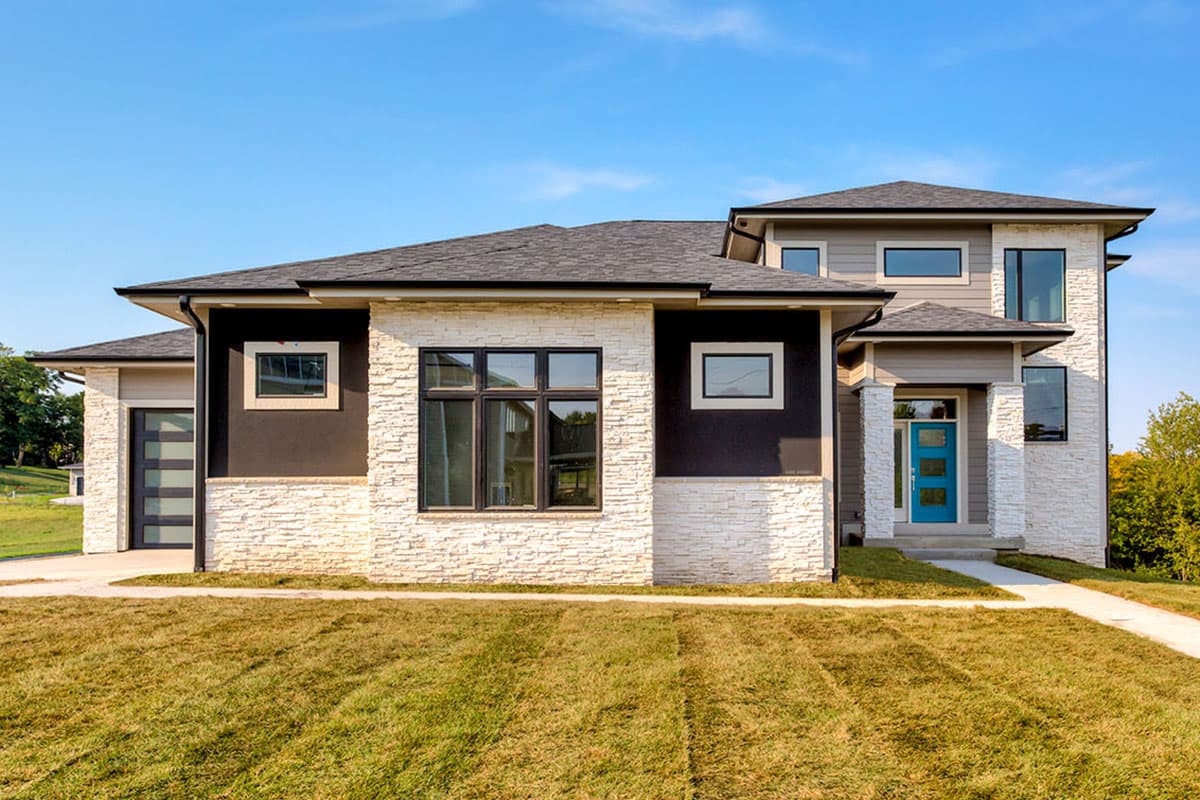 Modern house plan exterior with stacked stone, dark stucco, a glass garage door, and a blue front door.