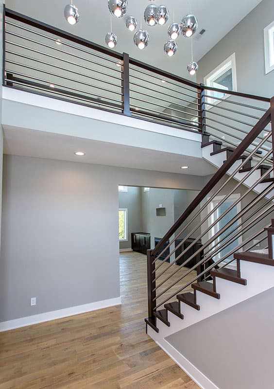 Modern interior view of a two-story home with floating stairs, horizontal railings, and a contemporary chandelier.