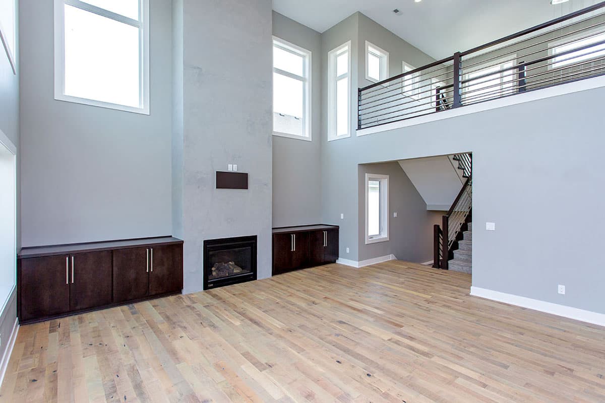 Interior rendering of a great room with a two-story ceiling, fireplace, built-in cabinets, and an open loft with metal railings.