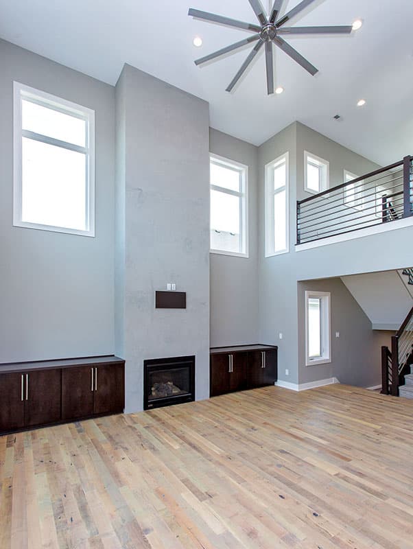 Great room with tall fireplace, dark wood cabinets, and a modern ceiling fan. Open to upper level with black railing.