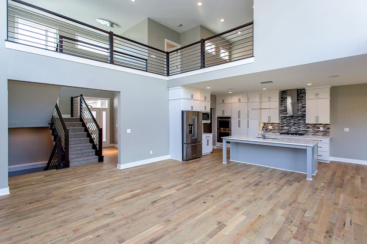 Interior view of a modern open-concept living area with a loft, kitchen island, white cabinets, and a prominent staircase.
