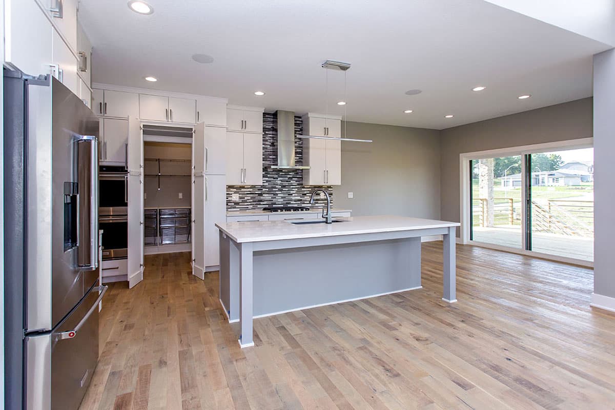 Modern kitchen with island, stainless steel appliances, pantry, and open access to a deck area with sliding glass doors.