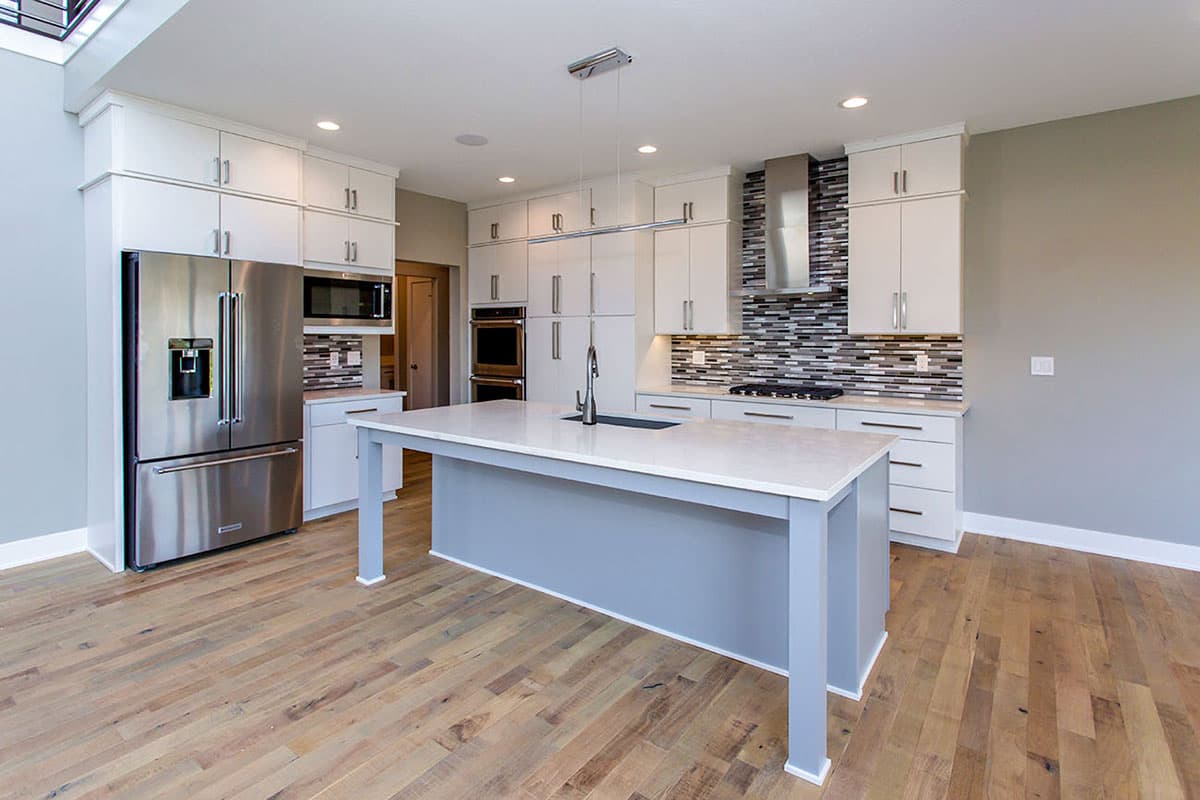 Modern kitchen with white cabinetry, stainless steel appliances, large island with sink, and multi-toned tile backsplash.