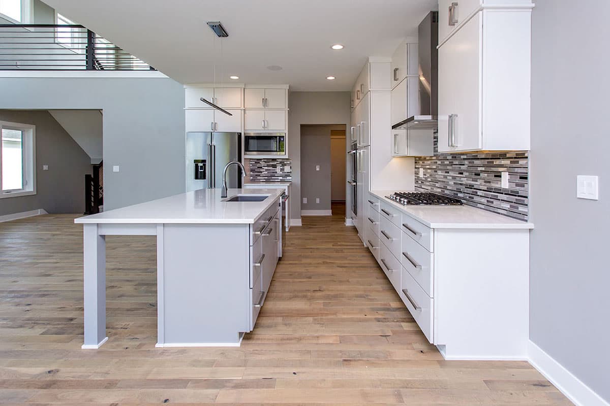 Modern kitchen with white cabinetry, large island, stainless steel appliances, and glass tile backsplash. Open to a living area with a loft above.