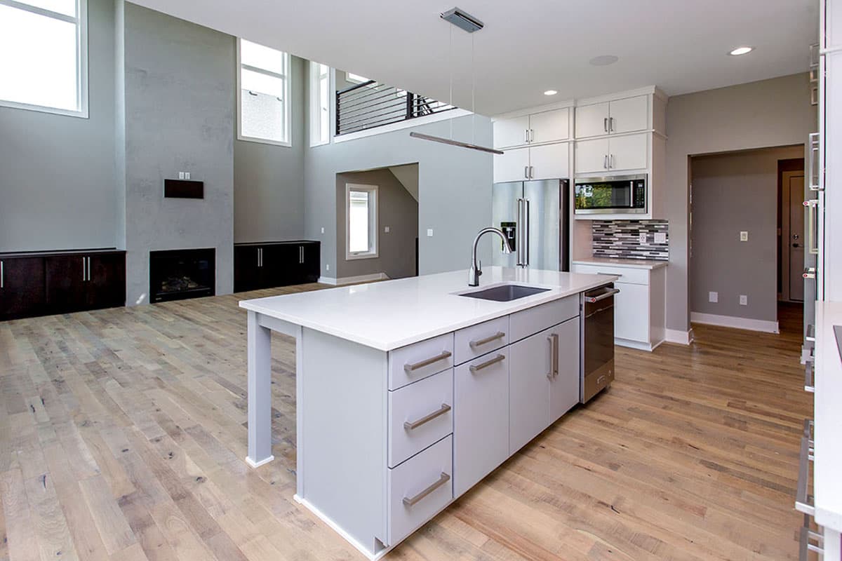 Open concept kitchen with island, stainless steel appliances, and fireplace in adjacent living space with high ceilings.