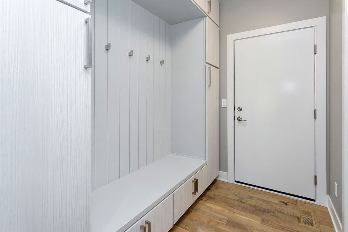 Mudroom with built-in white bench, vertical shiplap wall, coat hooks, storage cabinets, and a white door.
