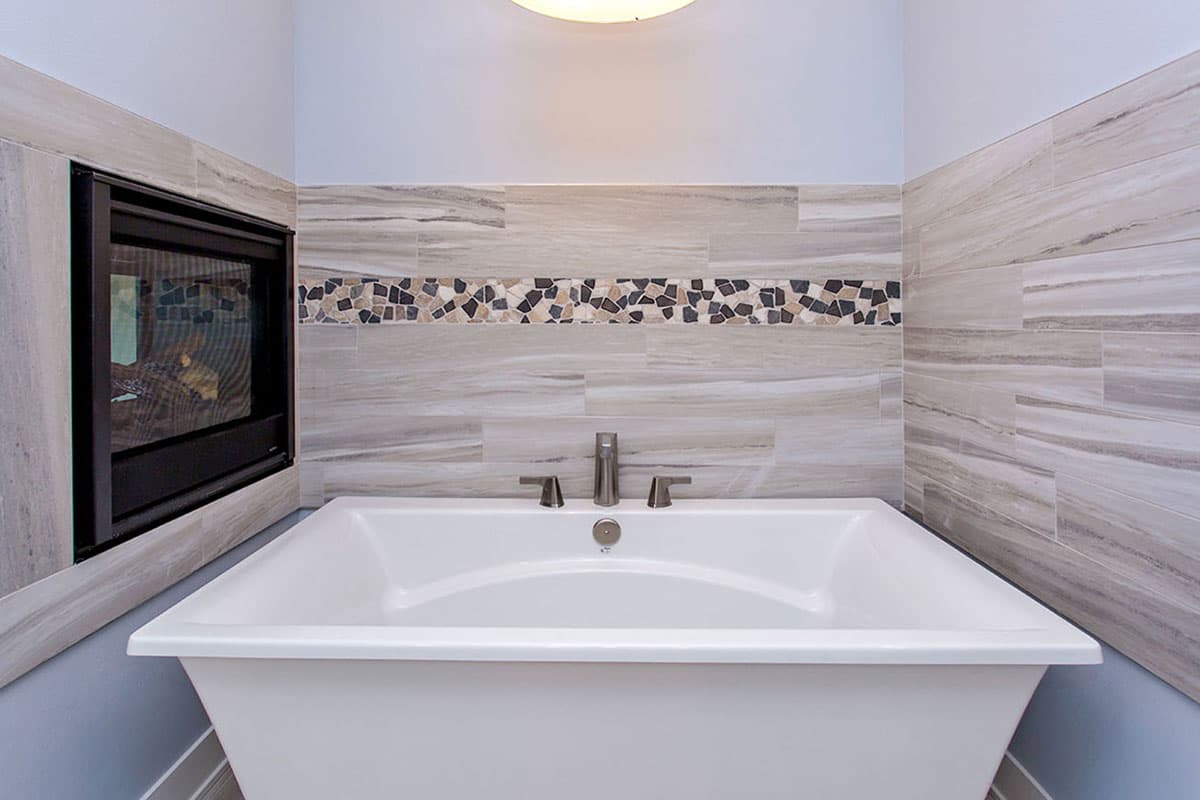Bathroom with freestanding tub, integrated fireplace, and horizontal wood-look tile with mosaic accent.