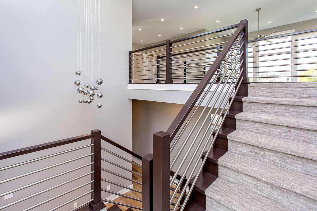 Interior view of a modern staircase with dark wood and brushed nickel railings, carpeted treads, and a chandelier.