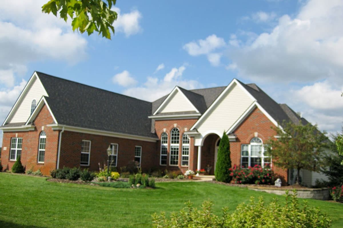 Brick house plan exterior with gables, arched windows, and an arched entryway supported by columns.