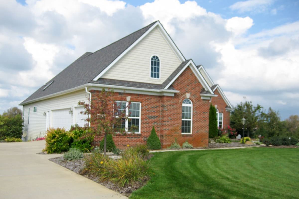 House plan exterior showing a two-story brick home with attached garage, gables, and arched dormer window.