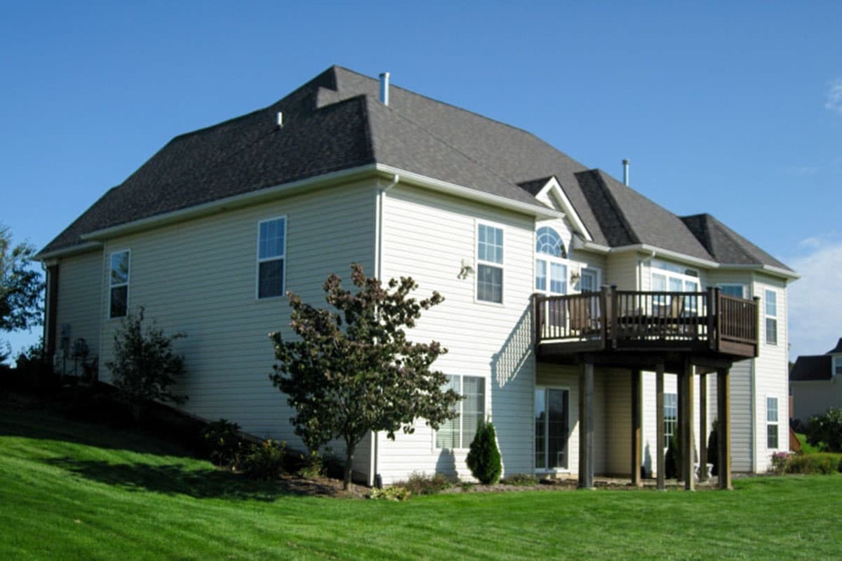 House plan exterior with light siding, gabled roof, and elevated deck with railing. Two stories visible.