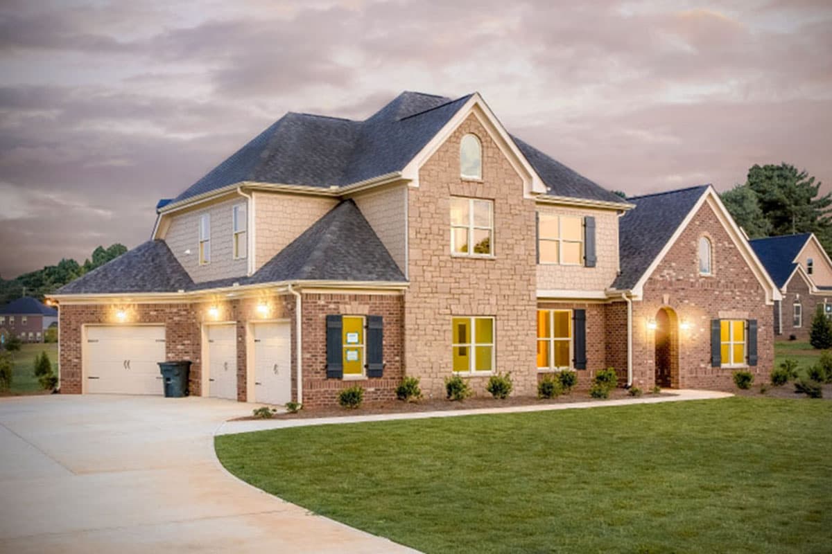 House plan exterior. Two-story brick and stone house with gabled roof, three-car garage, and arched entry door. Shutters on windows.