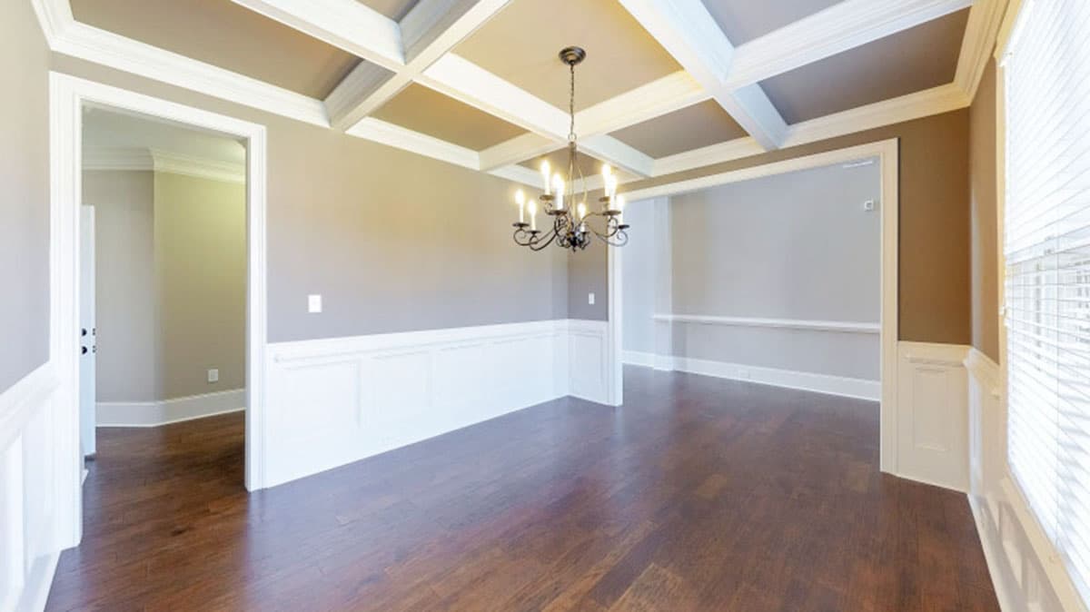 Interior view of dining room with coffered ceiling, wainscoting, chandelier, and hardwood floors.