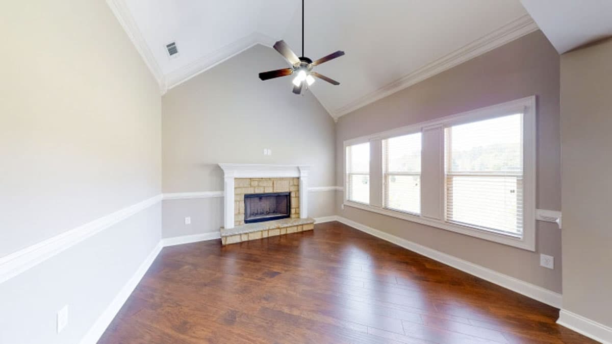 Interior rendering of a room with a stone fireplace, vaulted ceiling, ceiling fan, and large windows.