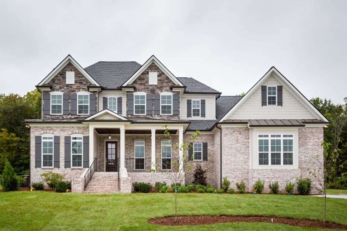 Two-story house plan exterior with multiple gables, front porch with columns, and brick facade with shutters.
