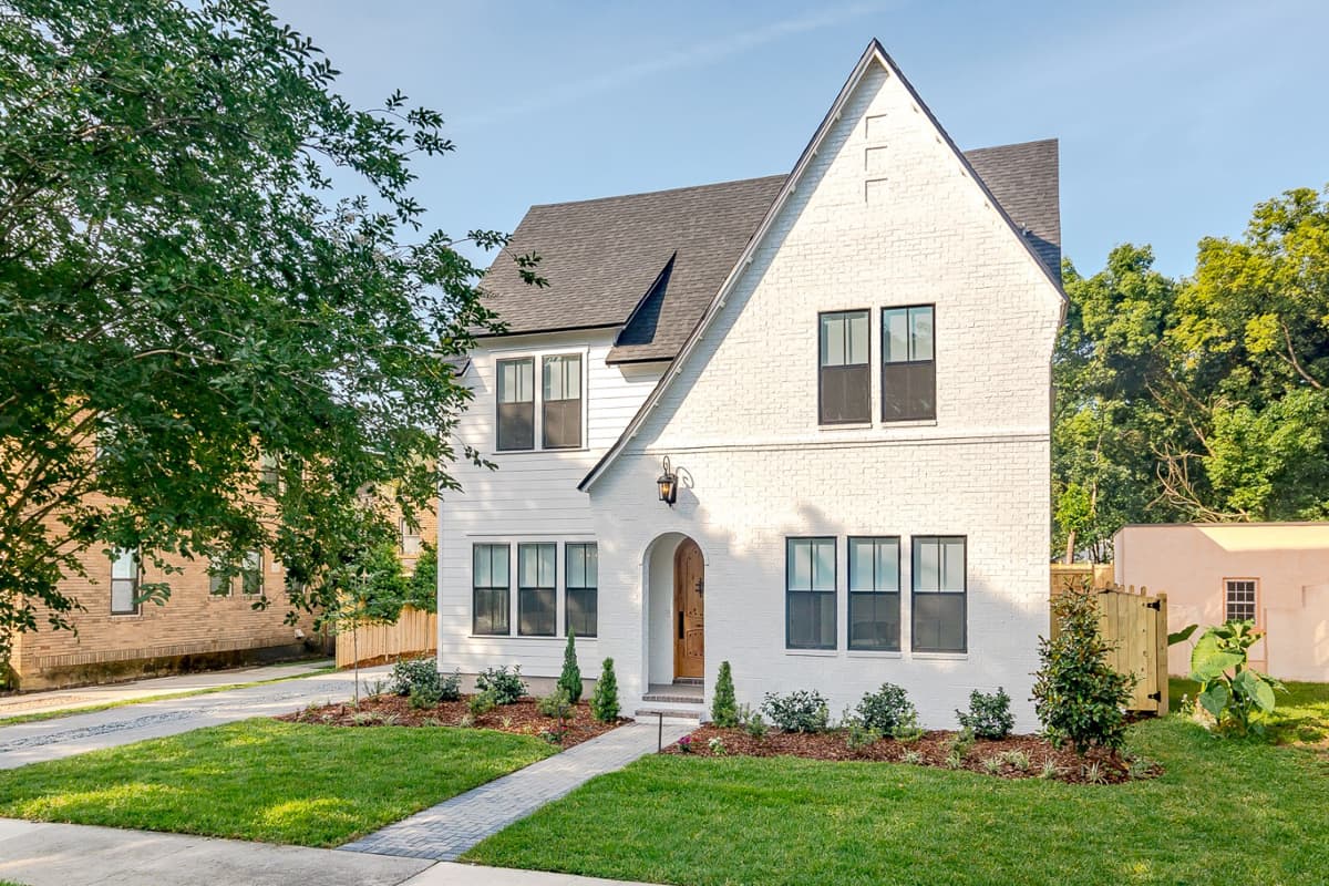House plan exterior, two stories, white brick and siding, gabled roof, arched entry with wood door, multiple windows.