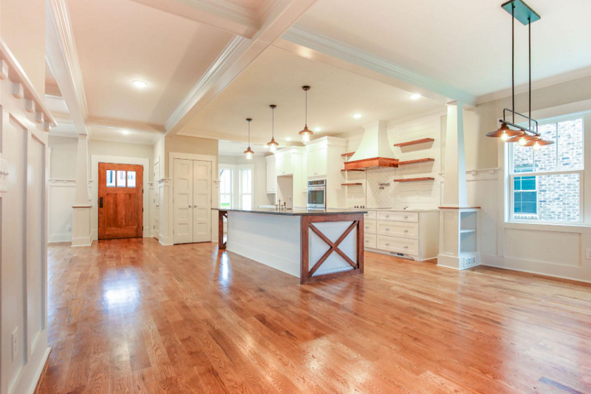 Open concept interior with wooden front door, kitchen island with X-brace detail, white cabinetry, and hardwood floors.