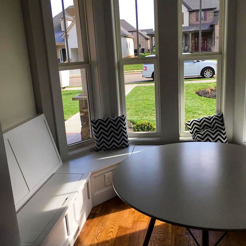 Breakfast nook with built-in storage bench, bay windows, and round table.